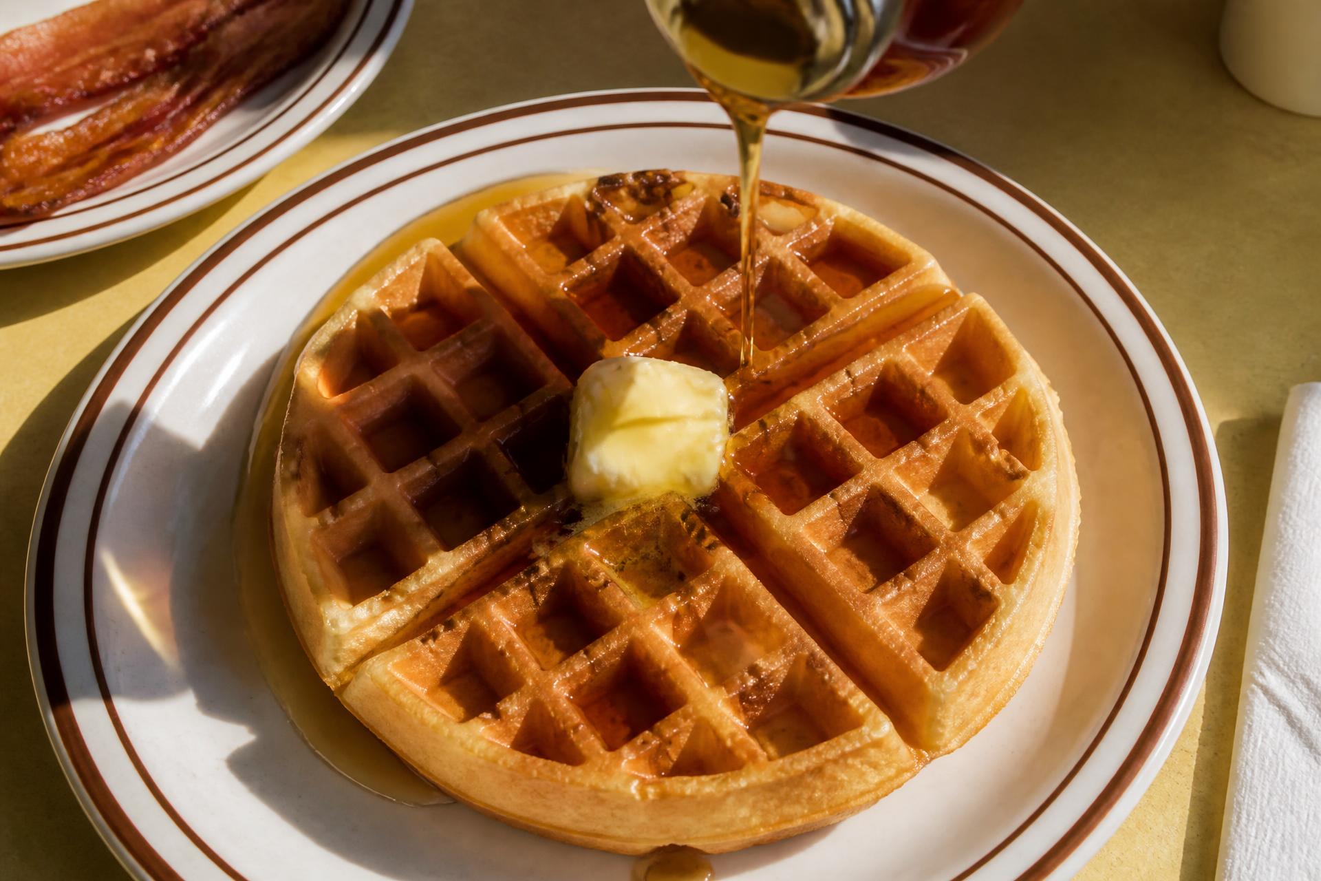 Golden Belgian waffle with butter and warm maple syrup on a diner plate