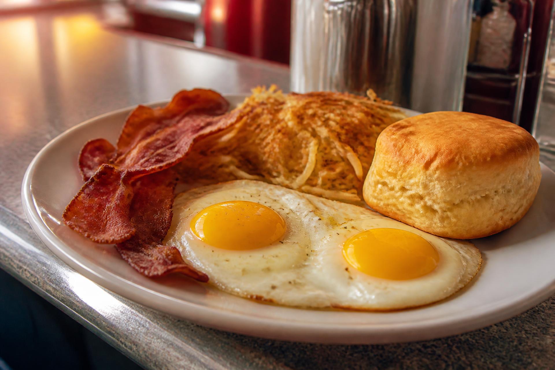 Two sunny-side up eggs, crispy bacon, hashbrowns and a biscuit on a diner counter