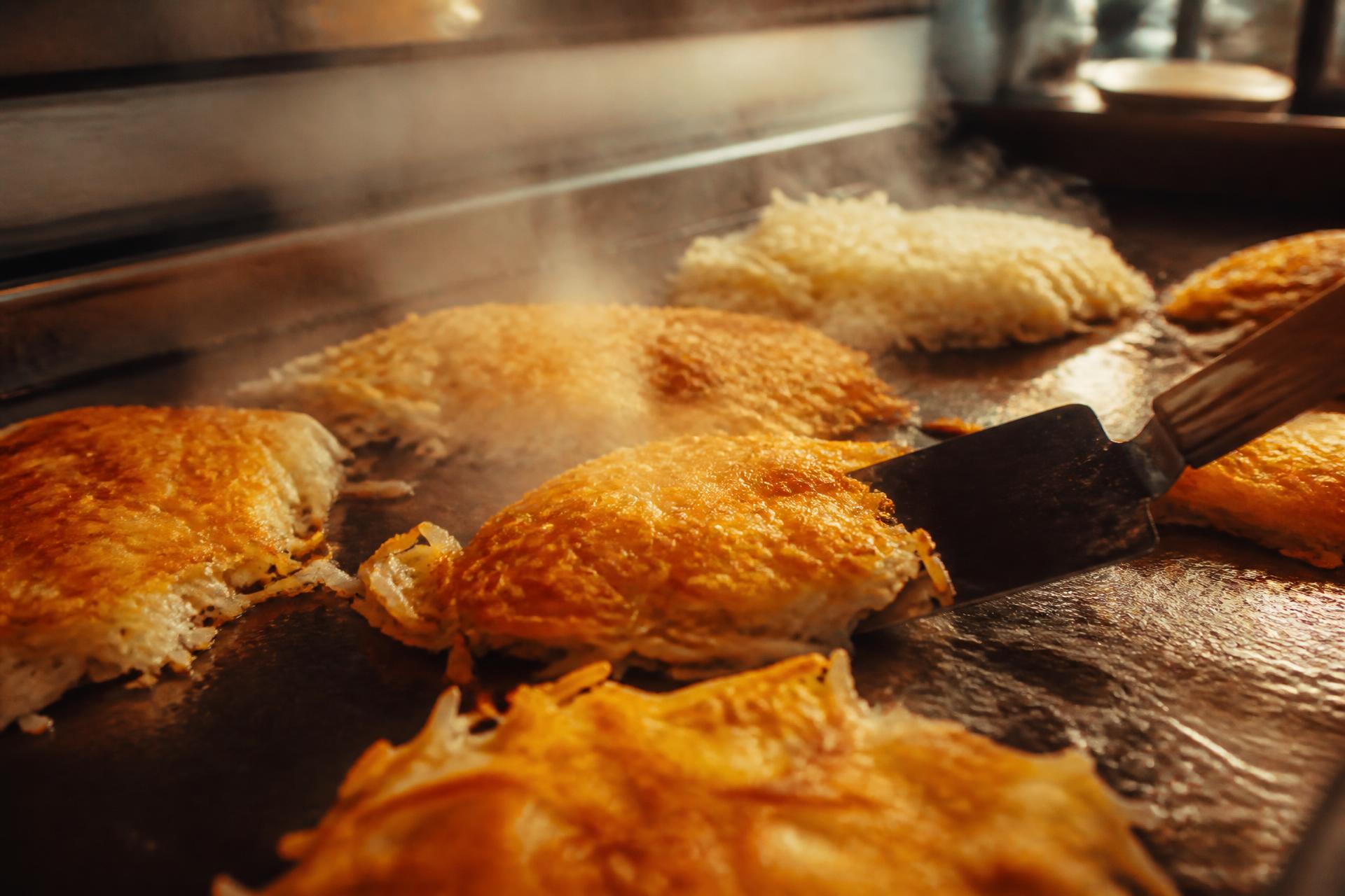Golden crispy hashbrowns steaming on a hot flat-top griddle